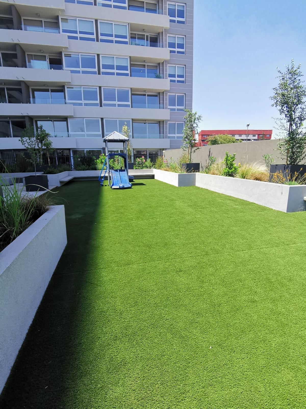 Jardín con pasto y juegos infantiles en Activa Plaza Chacabuco