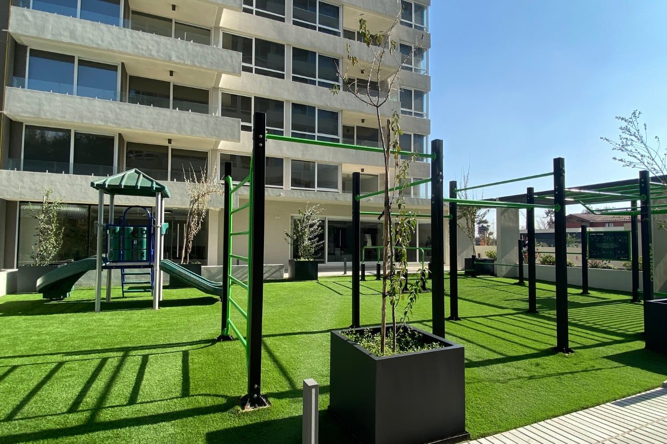 Juegos infantiles y máquinas de ejercicio sobre pasto frente a la torre de Mirador Activa